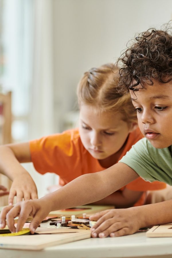 african american kid playing with didactic material near children and teacher in montessori school