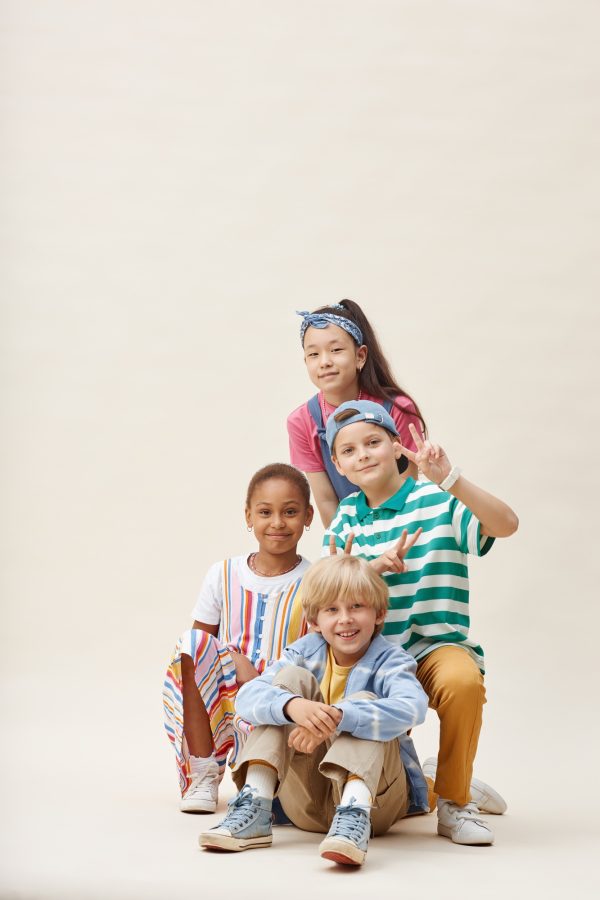 Four Smiling Children in Colorful Clothes Posing together Showing V Sign in Studio